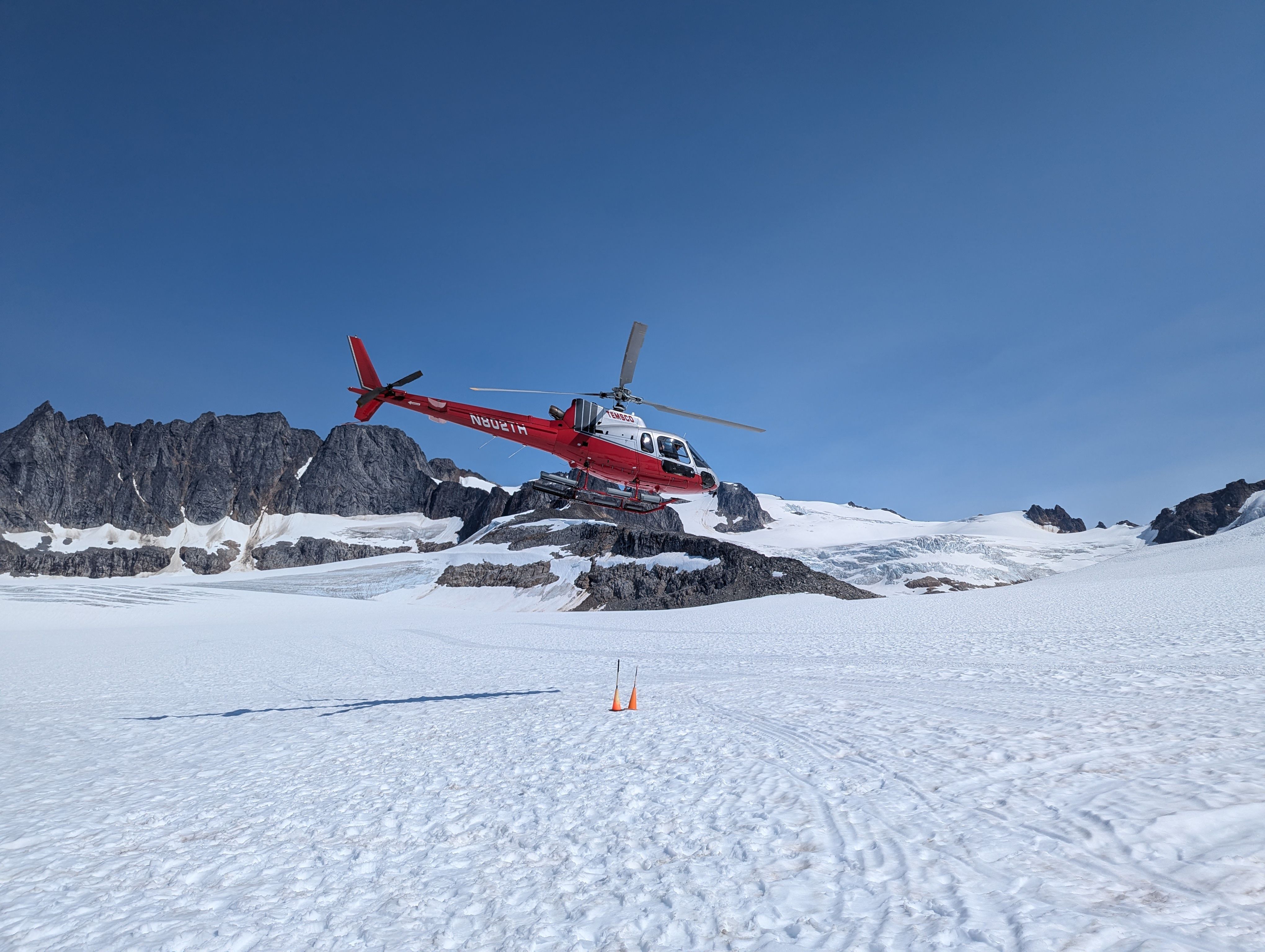 Red helicopter flying over a snowy glacier landscape in Alaska on an arctic helicopter tour