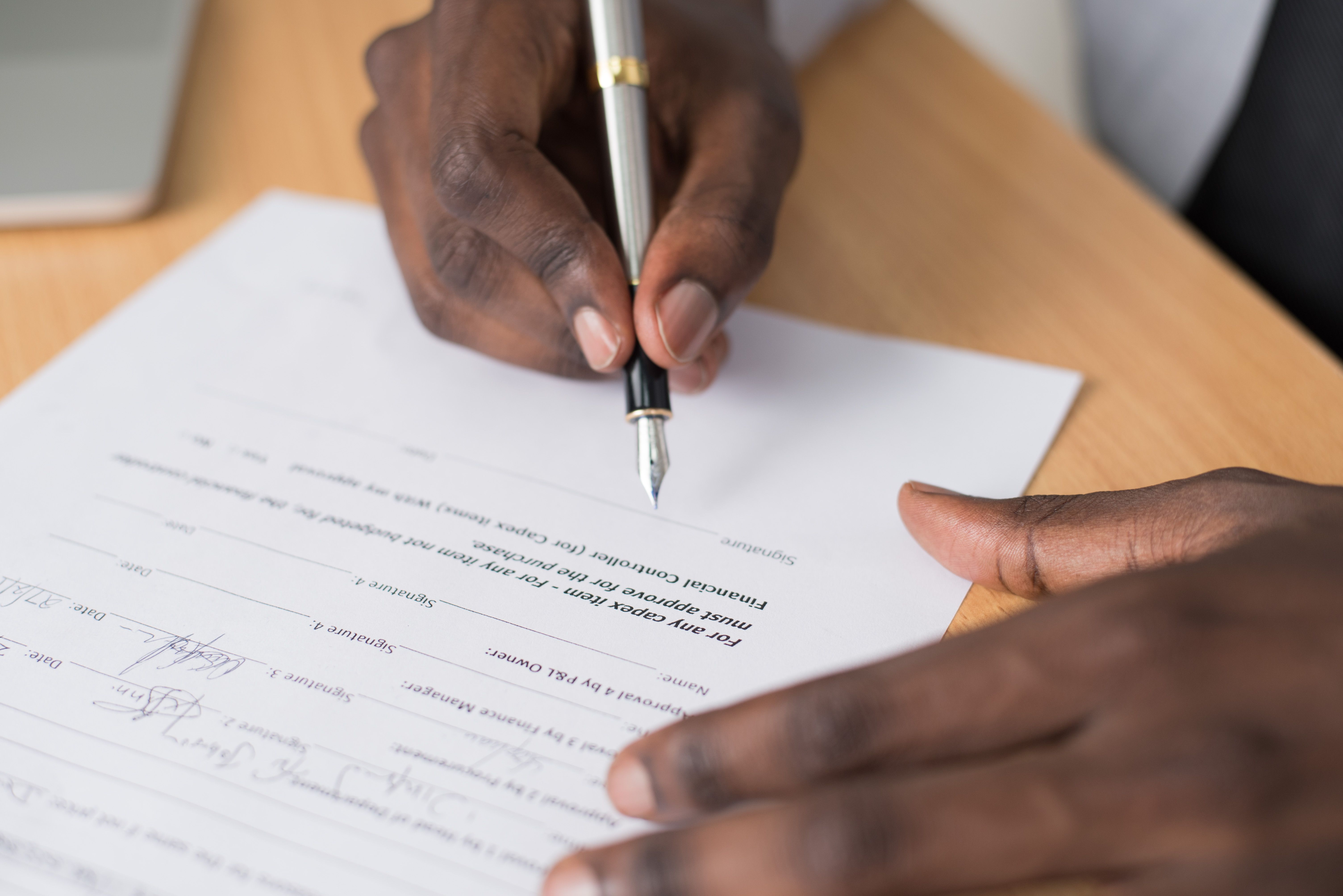 Close-up of hands signing a formal document, representing clear funding agreements and disclosure.